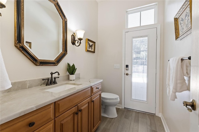 bathroom featuring baseboards, wood finished floors, toilet, and vanity