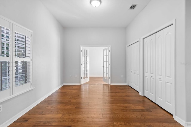 unfurnished bedroom featuring baseboards, wood finished floors, visible vents, and two closets