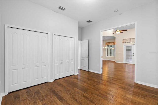 unfurnished bedroom featuring two closets, baseboards, wood finished floors, and visible vents