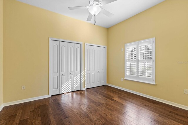 unfurnished bedroom featuring dark wood finished floors, two closets, a ceiling fan, and baseboards