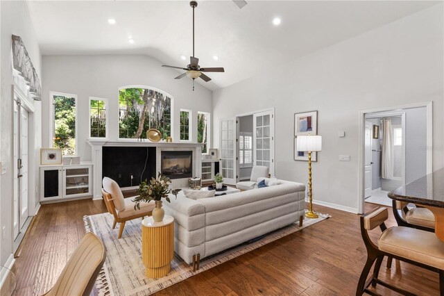 living area with wood finished floors, baseboards, a glass covered fireplace, high vaulted ceiling, and ceiling fan