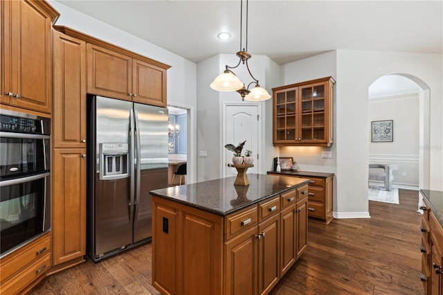 kitchen featuring dark wood finished floors, dobule oven black, glass insert cabinets, stainless steel fridge, and brown cabinetry
