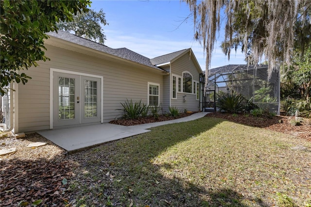 rear view of property featuring a lawn, a shingled roof, french doors, a patio, and a lanai