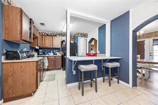 kitchen with a breakfast bar, kitchen peninsula, a textured ceiling, and light tile patterned floors