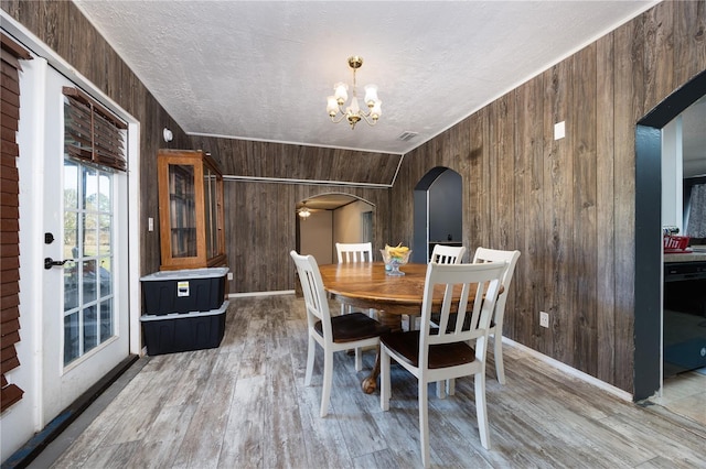 dining room featuring vaulted ceiling, light hardwood / wood-style flooring, a notable chandelier, and wood walls