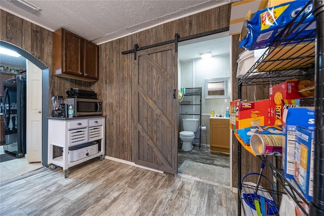 kitchen featuring black refrigerator, a textured ceiling, a barn door, and wood walls