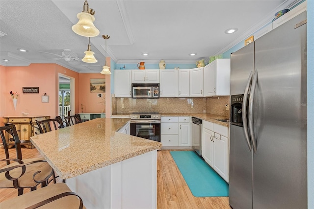 kitchen featuring white cabinets, decorative light fixtures, stainless steel appliances, and light stone countertops