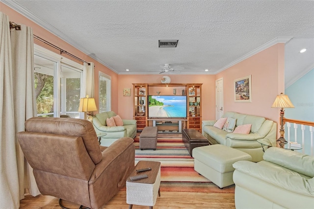 living room with light wood-type flooring, a textured ceiling, ceiling fan, and ornamental molding