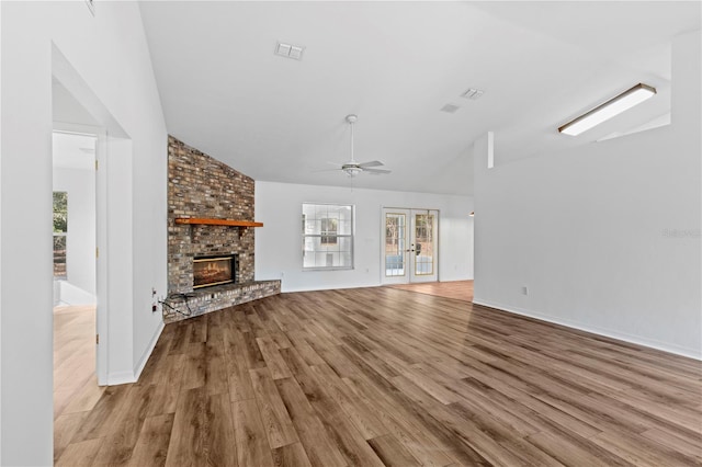 unfurnished living room with lofted ceiling, french doors, light hardwood / wood-style floors, ceiling fan, and a brick fireplace