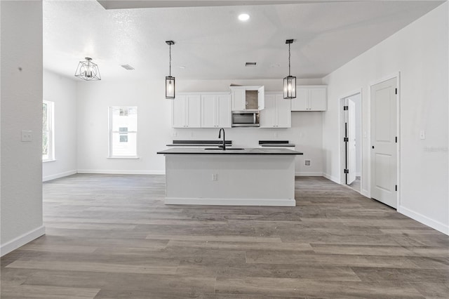 kitchen featuring white cabinetry, a kitchen island with sink, decorative light fixtures, and light wood-type flooring