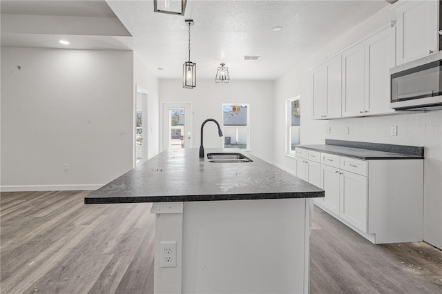 kitchen with a center island with sink, white cabinetry, sink, and hanging light fixtures