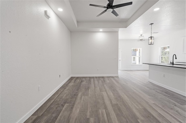 unfurnished living room with a textured ceiling, ceiling fan with notable chandelier, light hardwood / wood-style floors, and sink