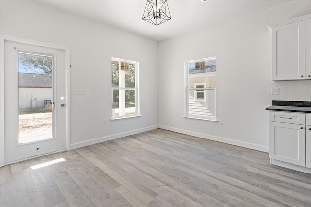 unfurnished dining area featuring a healthy amount of sunlight, light hardwood / wood-style floors, and an inviting chandelier