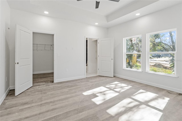 unfurnished bedroom featuring ceiling fan, a spacious closet, a tray ceiling, and a closet