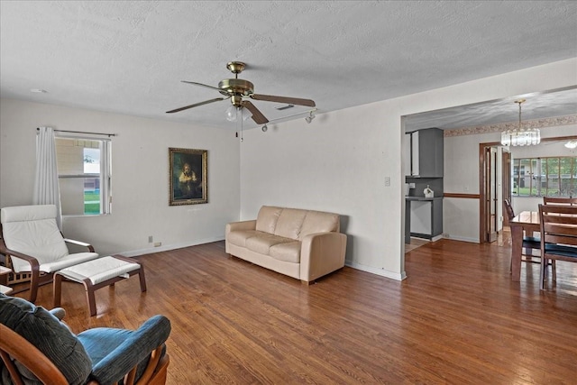 living room featuring wood-type flooring, ceiling fan with notable chandelier, and a textured ceiling