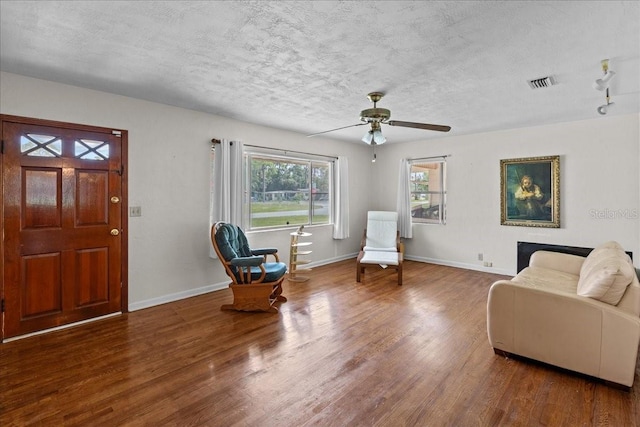 living area featuring hardwood / wood-style flooring, ceiling fan, and a textured ceiling