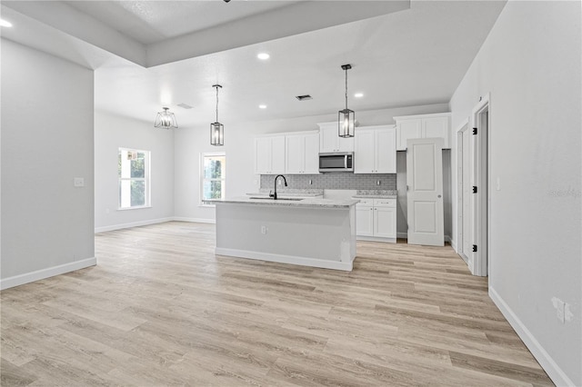 kitchen with sink, a kitchen island with sink, pendant lighting, decorative backsplash, and white cabinets