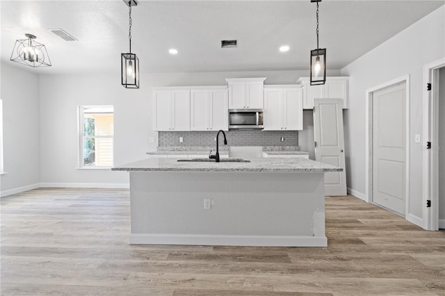 kitchen with light stone countertops, sink, pendant lighting, white cabinets, and an island with sink