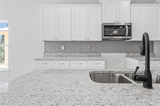 kitchen with light stone counters, white cabinetry, sink, and tasteful backsplash