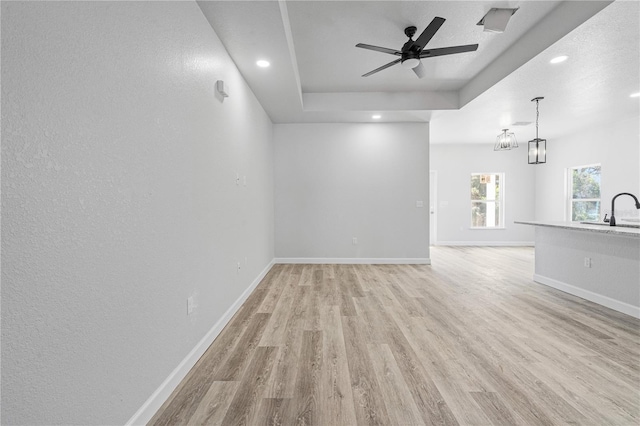 unfurnished living room featuring ceiling fan, sink, a raised ceiling, a textured ceiling, and light wood-type flooring