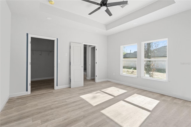 unfurnished bedroom featuring a raised ceiling, ceiling fan, a spacious closet, light wood-type flooring, and a closet