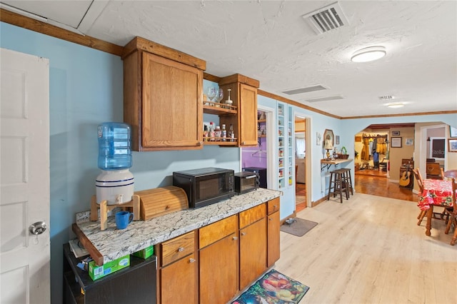 kitchen featuring light stone counters, ornamental molding, light hardwood / wood-style floors, and a textured ceiling