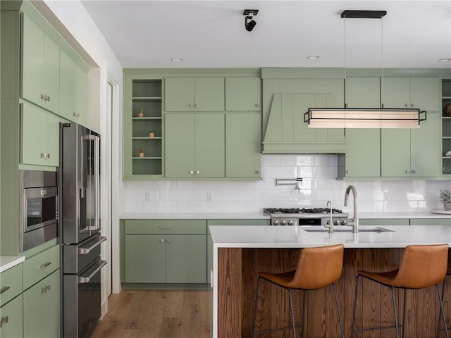 kitchen featuring sink, a kitchen breakfast bar, green cabinets, decorative backsplash, and appliances with stainless steel finishes