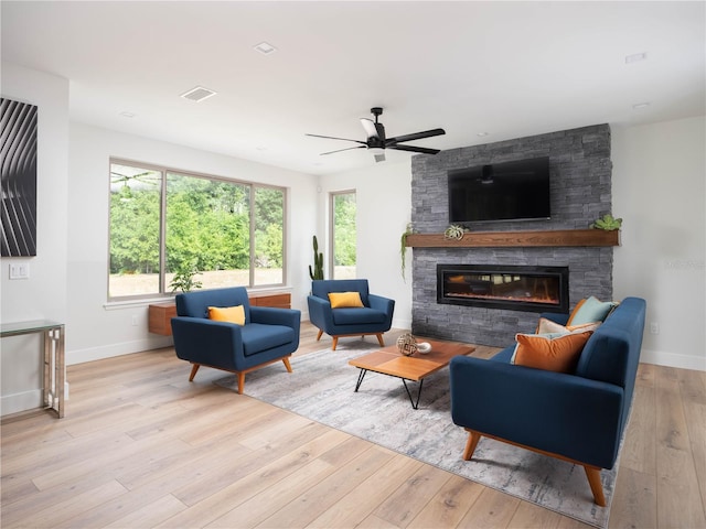 living room featuring a stone fireplace, ceiling fan, and light hardwood / wood-style floors