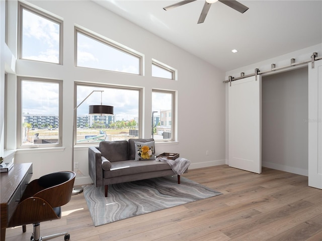 living area featuring ceiling fan, a barn door, light wood-type flooring, and vaulted ceiling