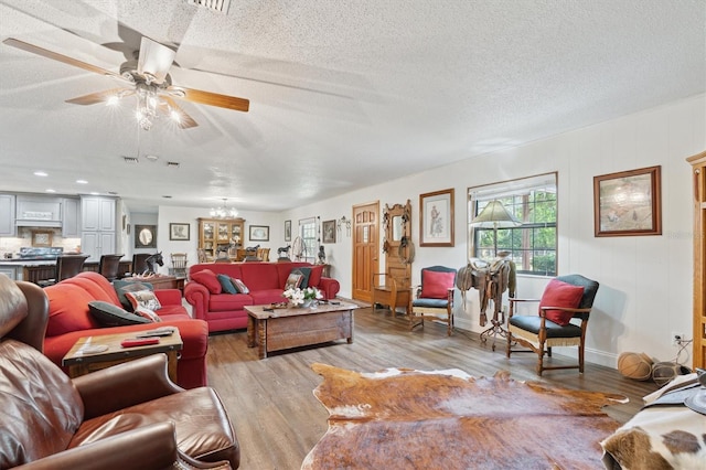 living room featuring light wood-type flooring, a textured ceiling, and ceiling fan with notable chandelier