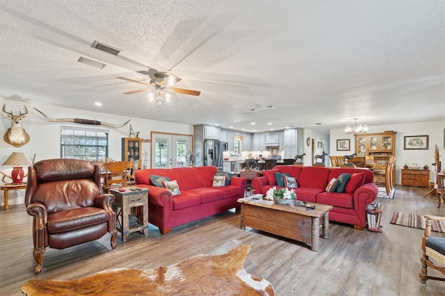 living room featuring french doors, ceiling fan with notable chandelier, light hardwood / wood-style floors, and a textured ceiling