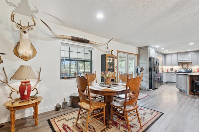 dining room featuring a healthy amount of sunlight, french doors, a textured ceiling, and light hardwood / wood-style flooring