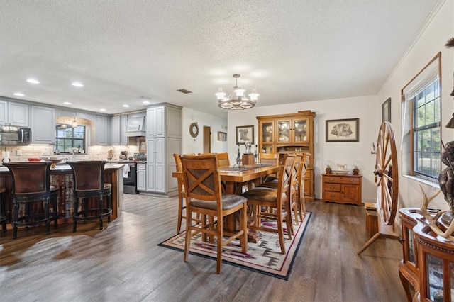 dining area with a textured ceiling, crown molding, dark wood-type flooring, and a chandelier