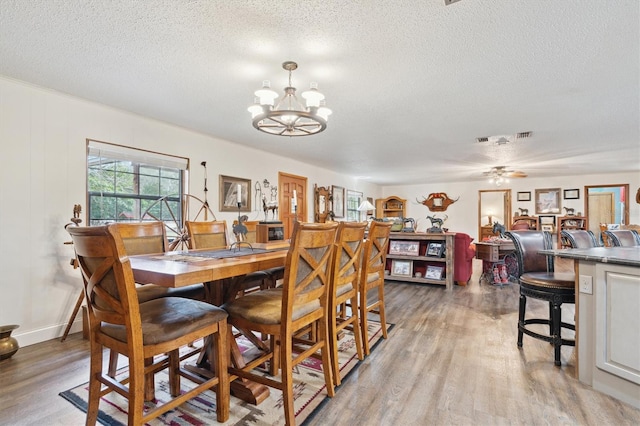 dining area with ceiling fan with notable chandelier, light hardwood / wood-style floors, and a textured ceiling