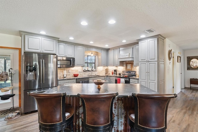 kitchen featuring appliances with stainless steel finishes, a kitchen island, custom range hood, and gray cabinetry