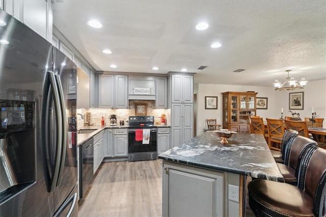 kitchen with decorative light fixtures, gray cabinets, appliances with stainless steel finishes, a notable chandelier, and a kitchen island