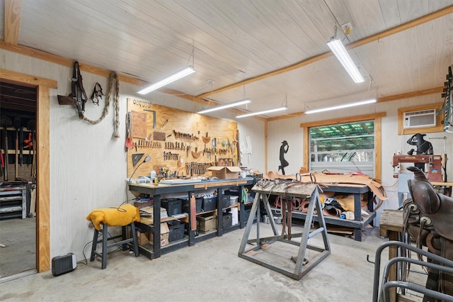 miscellaneous room featuring an AC wall unit, a workshop area, wooden walls, and concrete floors