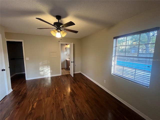 unfurnished bedroom featuring ensuite bath, ceiling fan, dark hardwood / wood-style flooring, a textured ceiling, and a walk in closet