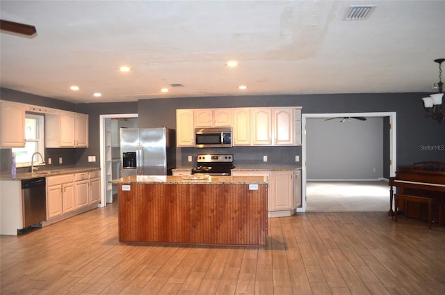 kitchen with light stone countertops, sink, stainless steel appliances, a kitchen island, and light wood-type flooring