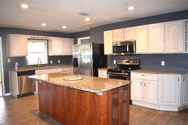 kitchen with light stone countertops, a center island, white cabinets, and stainless steel appliances