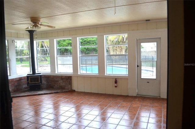 unfurnished sunroom with a wood stove and ceiling fan