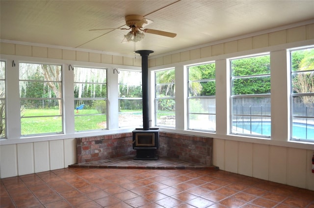 unfurnished sunroom featuring a wood stove and ceiling fan