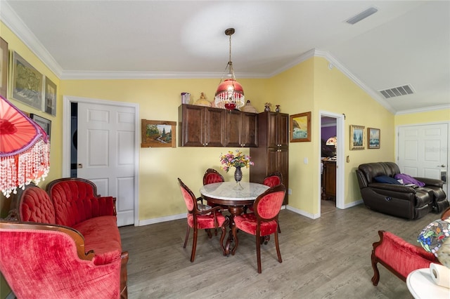 dining room featuring wood-type flooring, vaulted ceiling, and ornamental molding