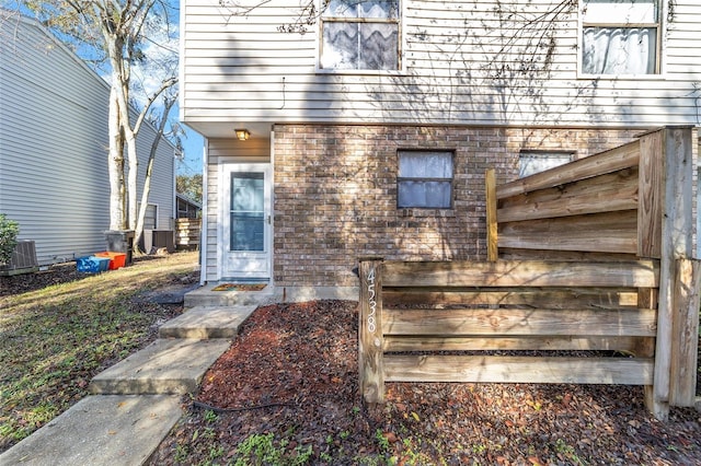 view of exterior entry with central AC and brick siding