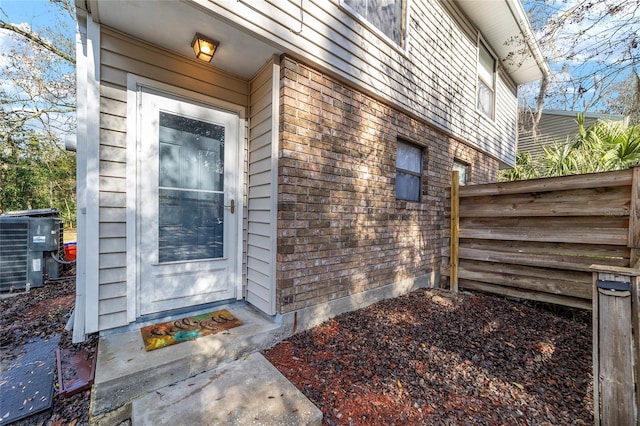 property entrance with fence, central AC, and brick siding