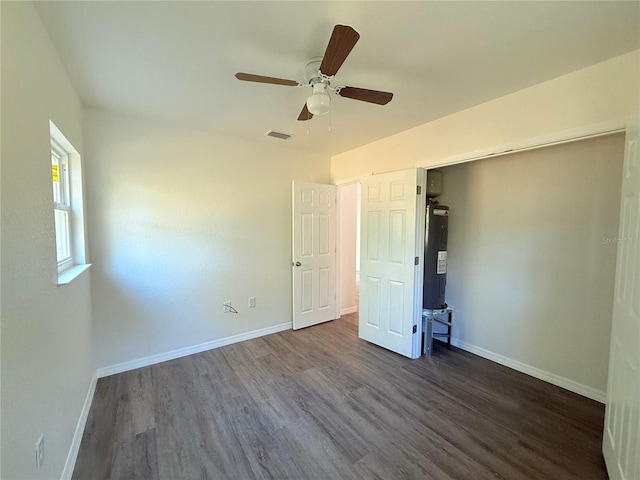 unfurnished bedroom with ceiling fan, dark wood-type flooring, and water heater