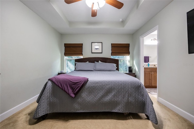 carpeted bedroom with ensuite bathroom, ceiling fan, multiple windows, and a tray ceiling