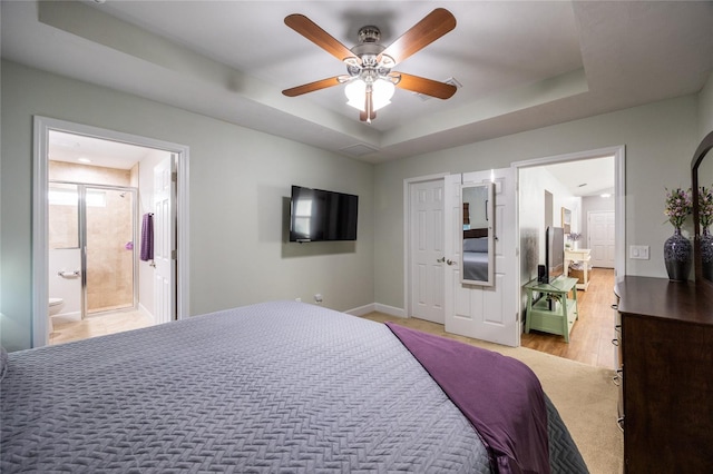 bedroom with a tray ceiling, connected bathroom, ceiling fan, and light hardwood / wood-style flooring