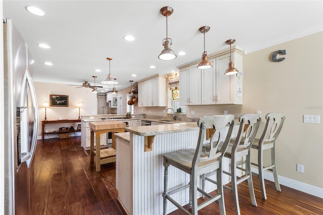 kitchen with kitchen peninsula, stainless steel appliances, ceiling fan, dark hardwood / wood-style floors, and hanging light fixtures