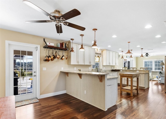 kitchen with a breakfast bar, white cabinets, hanging light fixtures, light stone countertops, and kitchen peninsula